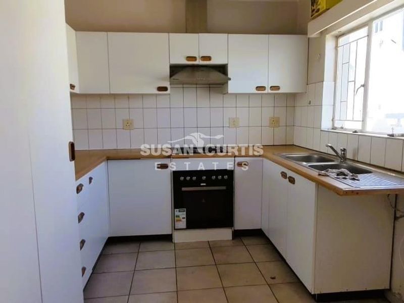 A functional kitchen featuring white cabinetry, laminate countertops, a built-in oven, and a double sink with a tiled backsplash.
