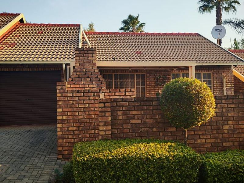 Front elevation of a brick townhouse featuring a tiled roof, paved driveway, and an integrated garage.