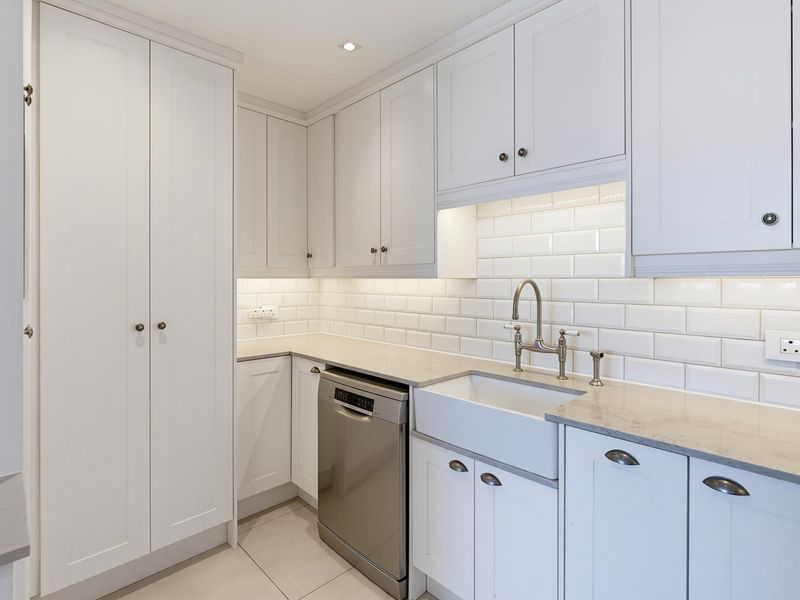 A modern, well-appointed scullery featuring white shaker cabinetry, stone countertops, a classic farmhouse sink, and a subway tile backsplash with integrated lighting.