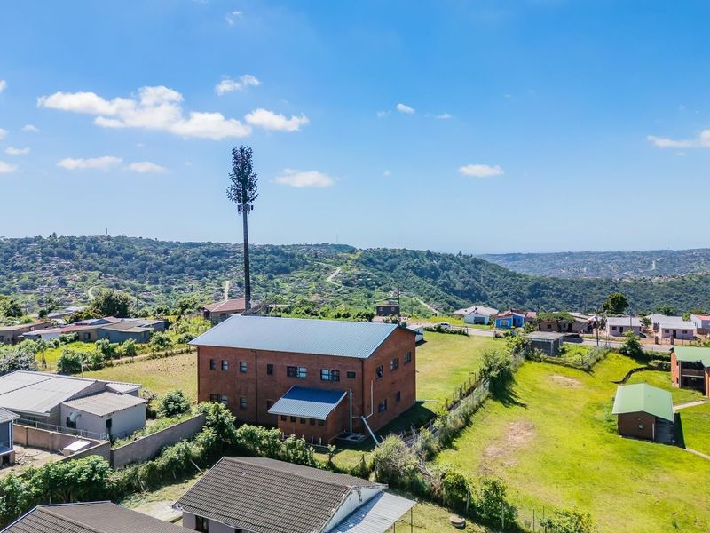 Aerial view of a residential property featuring a multi-story brick building with a metal roof, situated in a hilly landscape with surrounding neighborhood infrastructure.