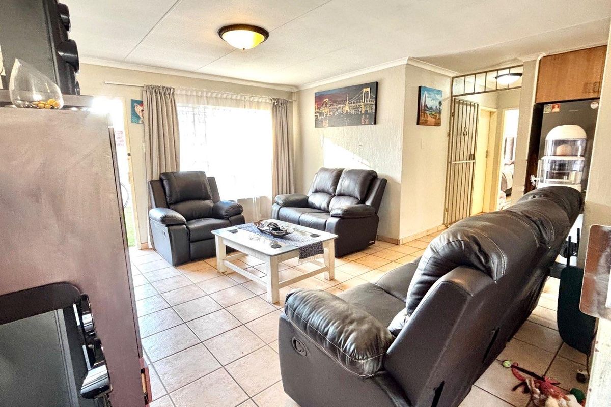 A living room featuring tiled flooring, a ceiling-mounted light fixture, and access to an adjacent hallway.