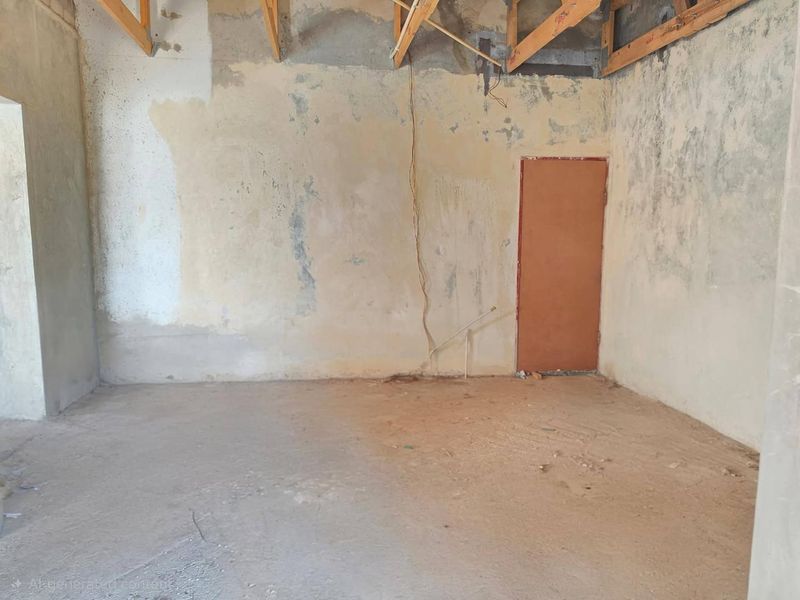 An unfinished interior space featuring exposed timber roof trusses, concrete flooring, and raw wall surfaces, presenting a blank canvas for renovation.