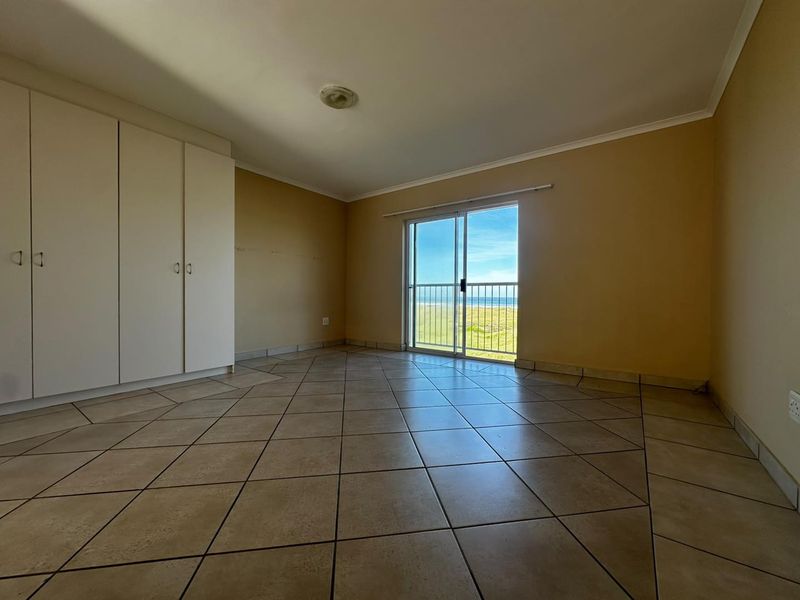 An empty bedroom featuring tiled flooring, built-in cupboards, and a sliding glass door that opens to a balcony with ocean views.