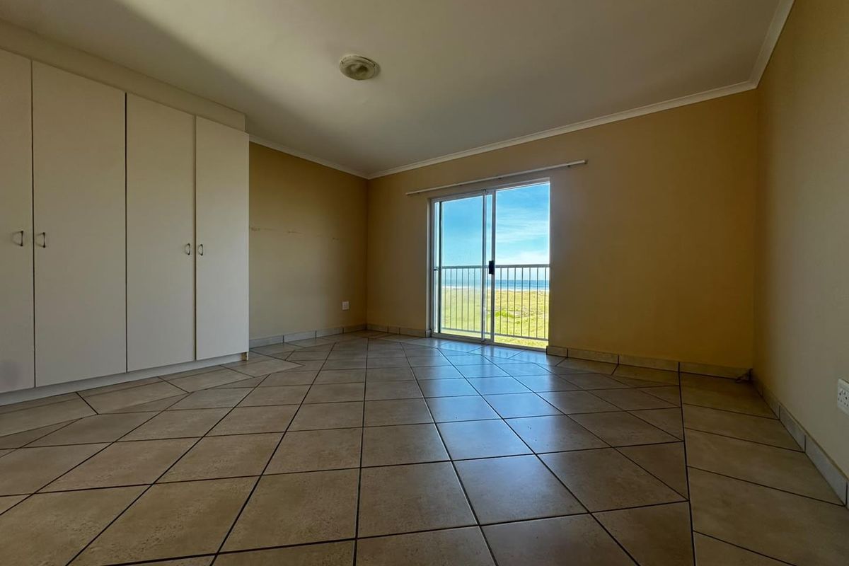An empty bedroom featuring tiled flooring, built-in cupboards, and a sliding glass door that opens to a balcony with ocean views.