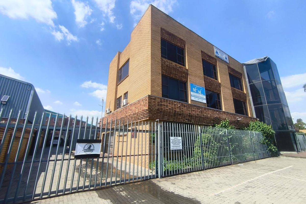 Front exterior view of a multi-story brick office building featuring a secure gated entrance, paved driveway, and a modern glass facade section.