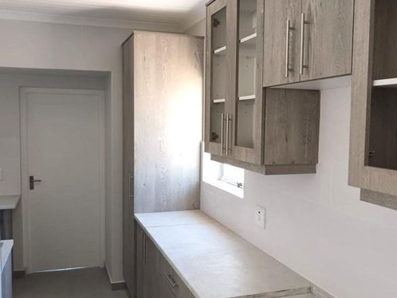 A modern, clean scullery featuring light wood-grain cabinetry, laminate countertops, and neutral tiled flooring with recessed ceiling lighting.