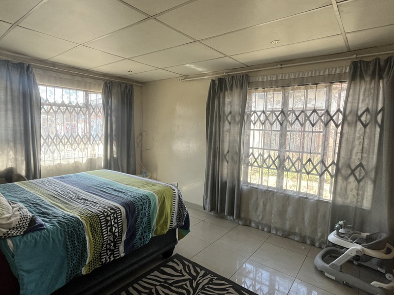A bedroom featuring tiled flooring, built-in wardrobe storage, and security gates on the windows, with a suspended ceiling finish.