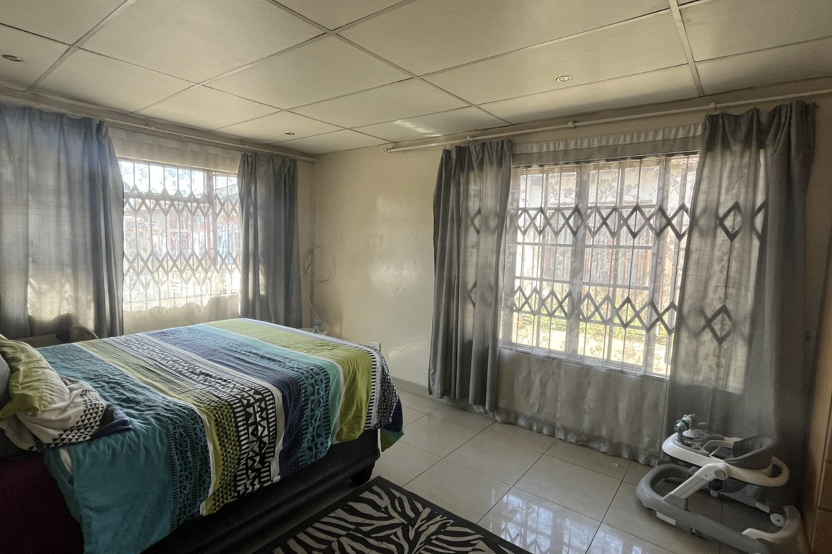 A bedroom featuring tiled flooring, built-in wardrobe storage, and security gates on the windows, with a suspended ceiling finish.