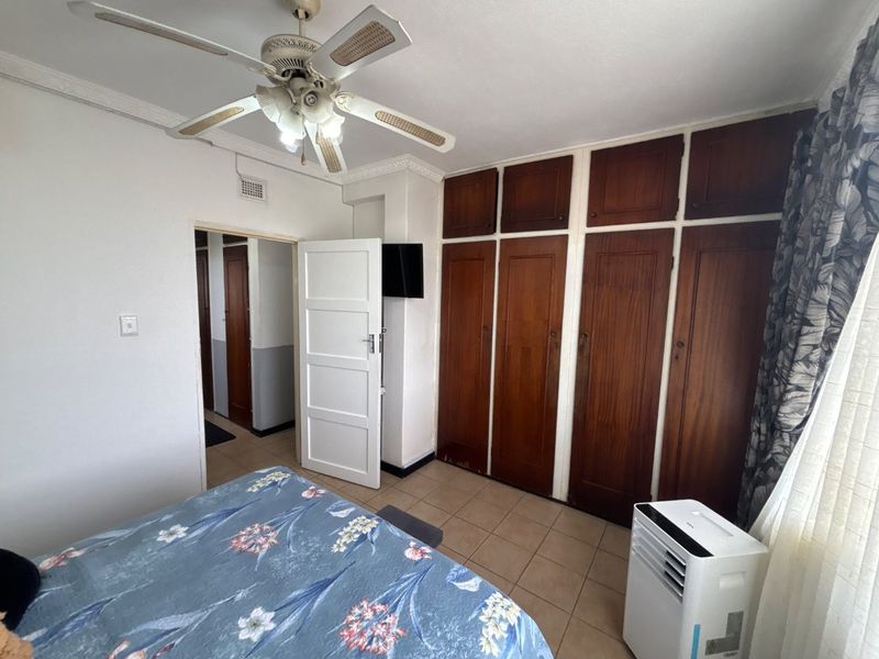 A bedroom featuring built-in wooden cupboards, tiled flooring, and a ceiling fan, offering a functional space with potential for modern updates.