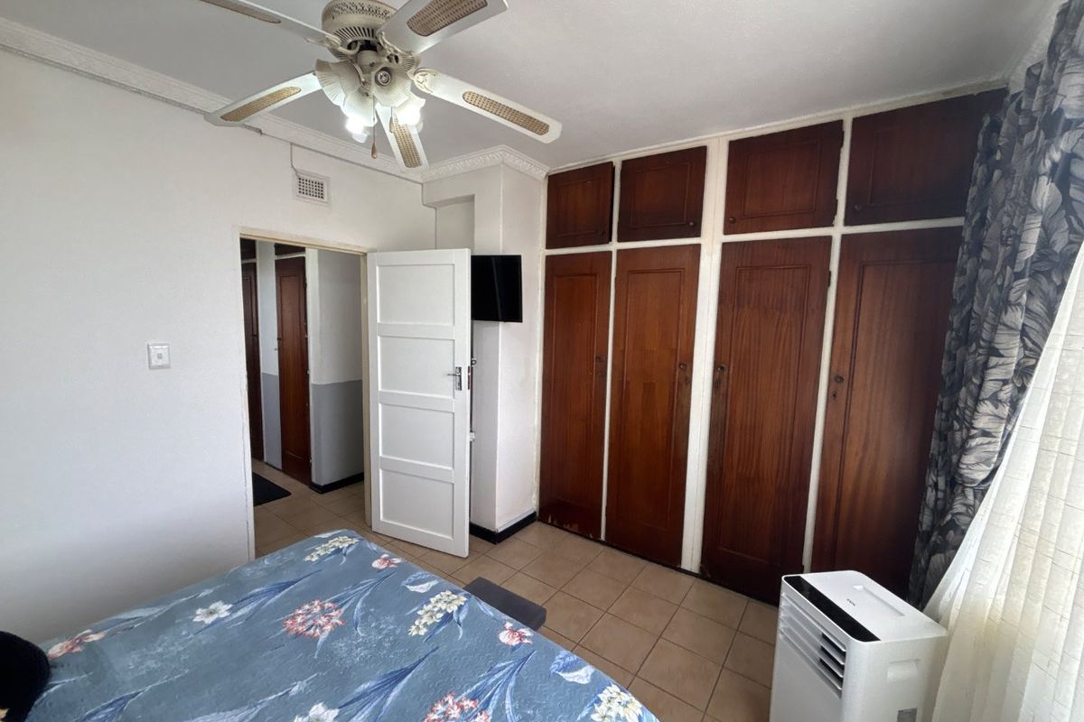 A bedroom featuring built-in wooden cupboards, tiled flooring, and a ceiling fan, offering a functional space with potential for modern updates.