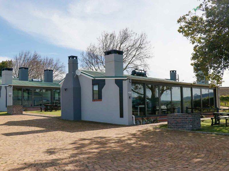 A well-maintained cottage exterior featuring extensive glass facades, multiple chimneys, and a spacious brick-paved driveway area.