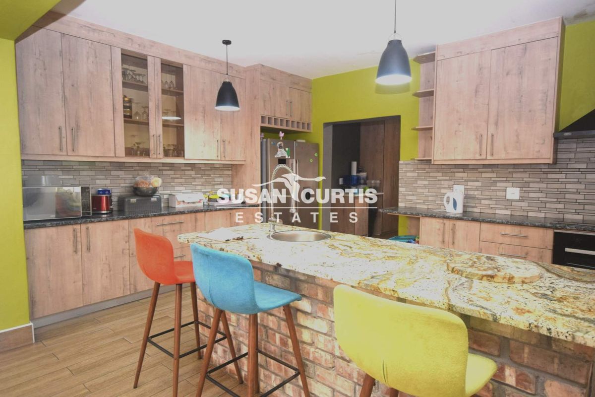 A functional kitchen featuring wood-look cabinetry, granite countertops, a brick-base island with a prep sink, and tiled backsplash.