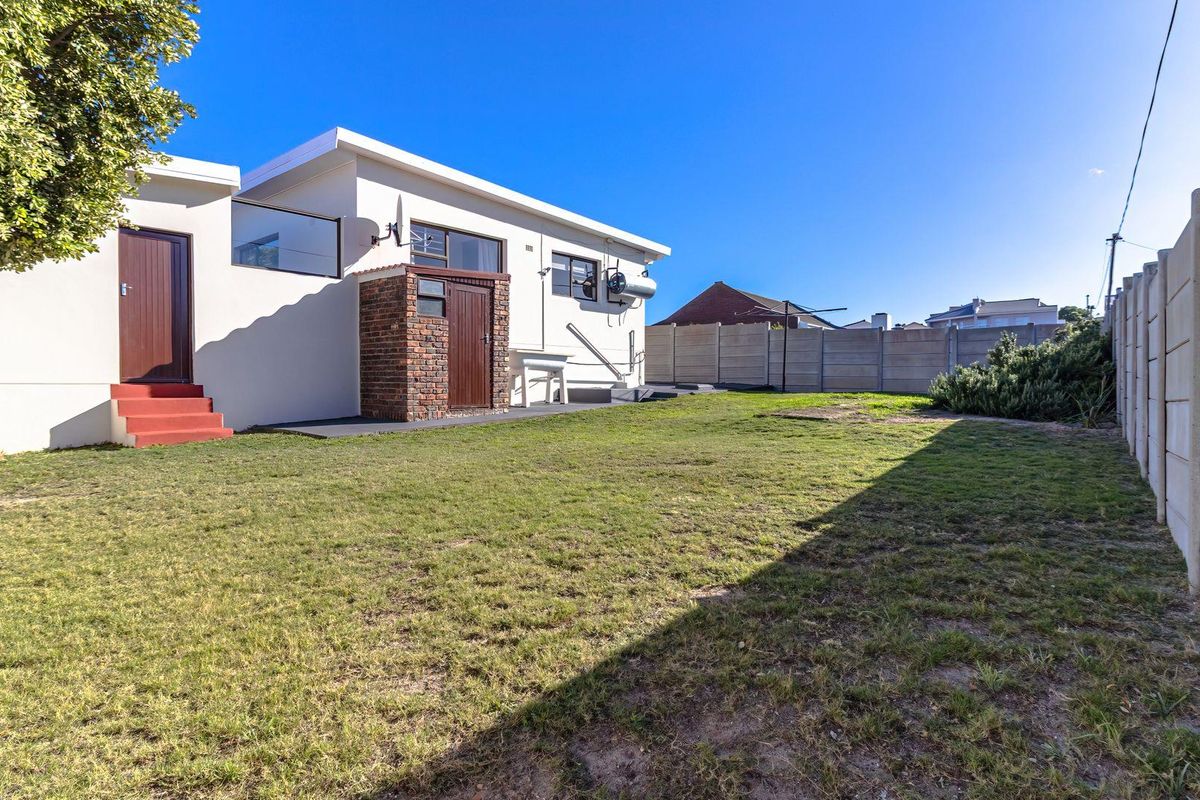 Rear view of the property featuring a spacious lawn, precast concrete boundary walls, and a solar water heater installation.
