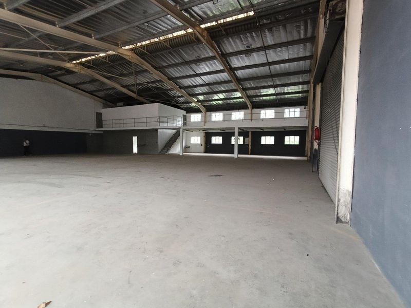 Spacious industrial warehouse featuring high ceilings with exposed steel trusses, concrete flooring, a mezzanine level, and a large roller shutter door for easy access.