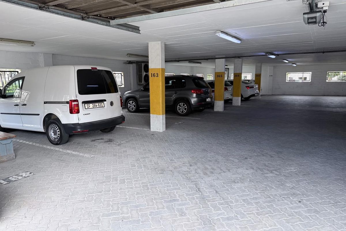 Covered parking garage area featuring paved flooring, structural support columns, and overhead fluorescent lighting.
