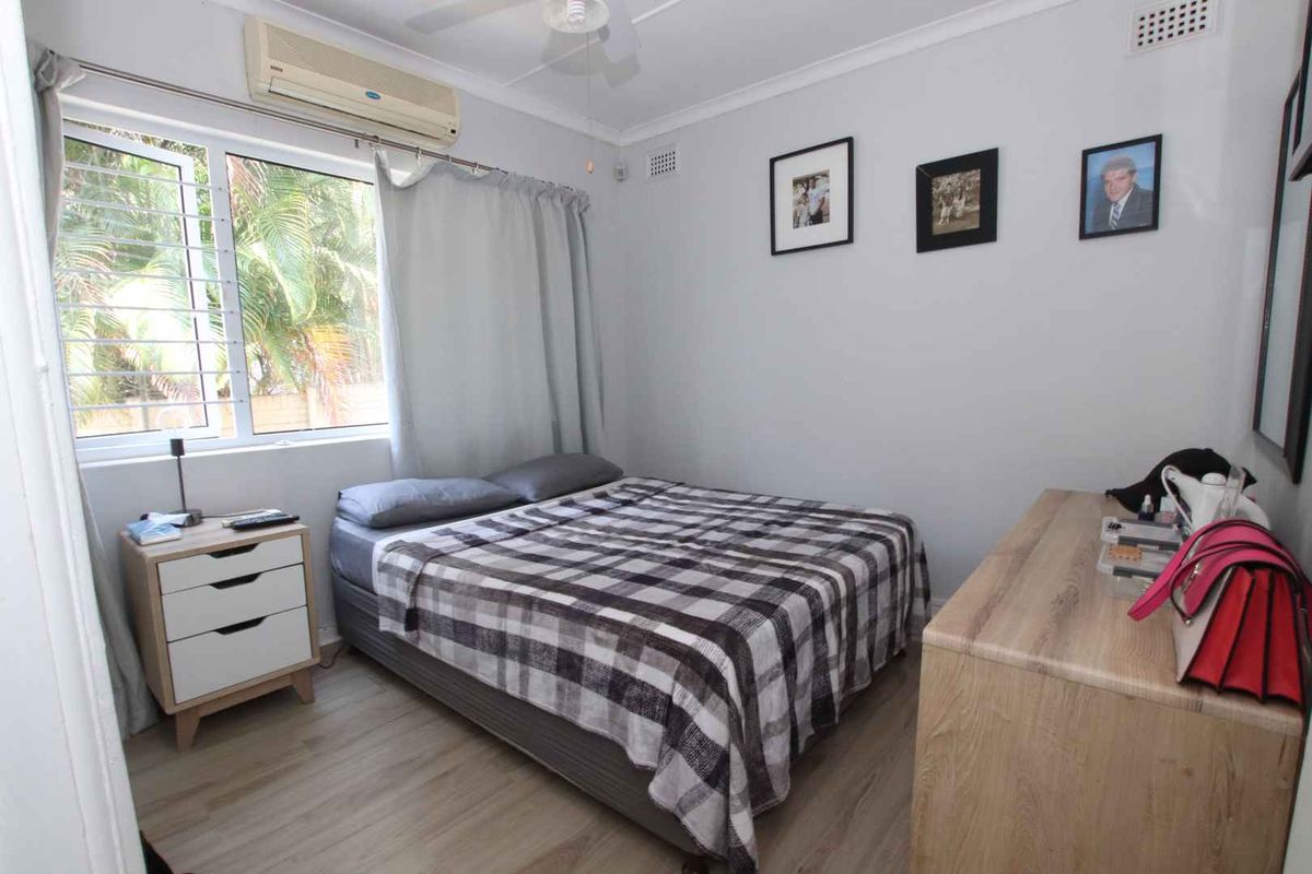 A bedroom featuring light wood-look flooring, a wall-mounted air conditioning unit, and a window with security bars.