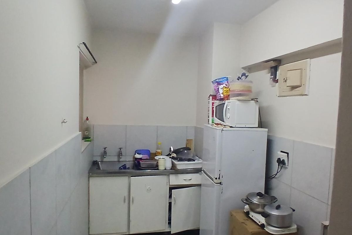 A compact kitchen area featuring a stainless steel sink, tiled splashback, and built-in cabinetry, requiring some maintenance and cosmetic updates.