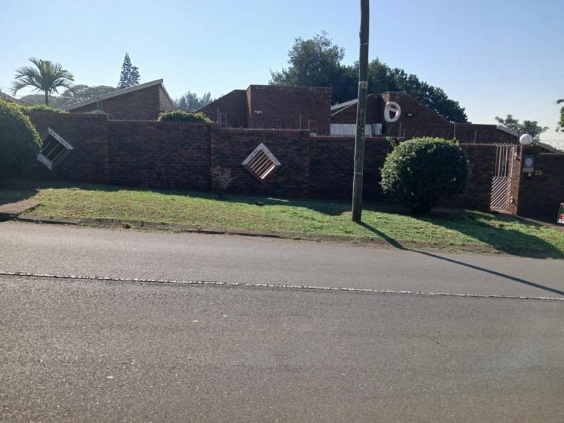 Street view of the property showing the brick boundary wall, security razor wire, and gated entrance from the road.
