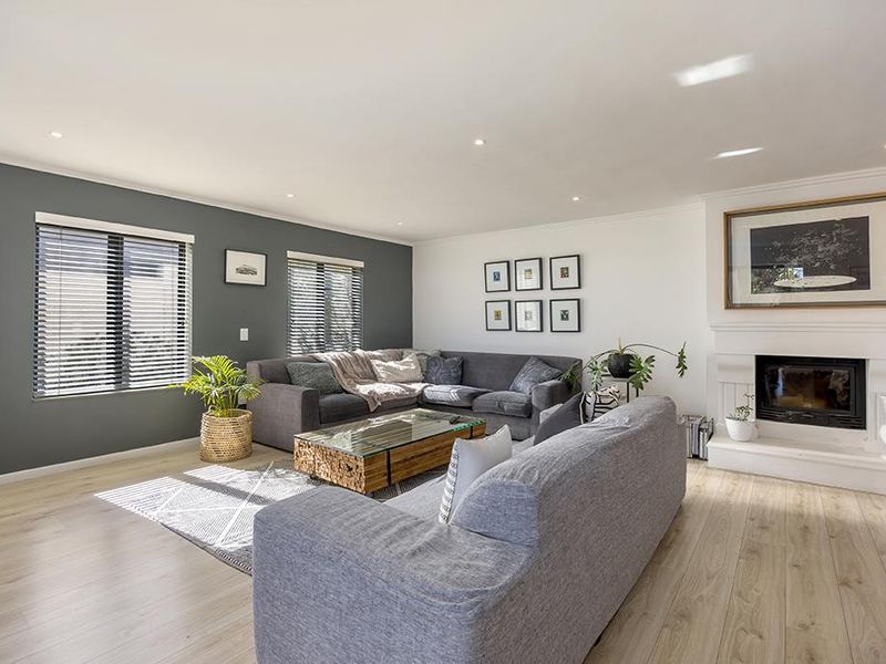 A bright and well-maintained living room featuring a fireplace, modern laminate flooring, and recessed downlights, creating a comfortable and inviting atmosphere.