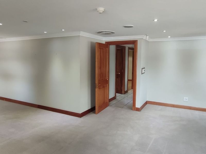 Spacious, empty office area featuring recessed downlighting, timber door frames, and neutral wall finishes, suitable for a professional workspace setup.