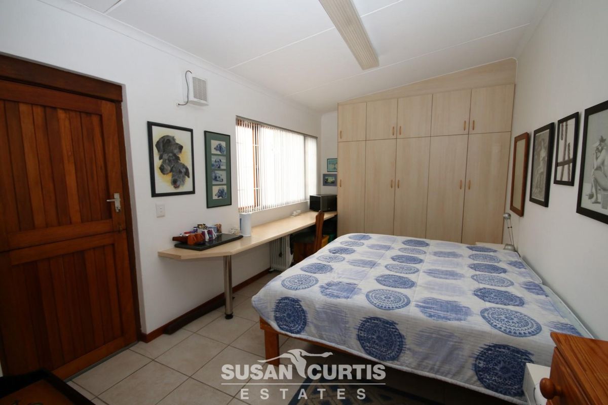 A functional bedroom featuring built-in light wood cabinetry, a fitted desk area, tiled flooring, and a solid timber door.