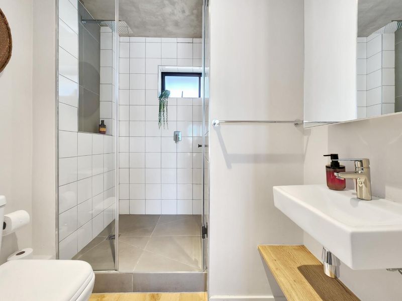 Modern bathroom featuring a walk-in shower with glass screen, wall-mounted basin, and contemporary tiled finishes with an exposed concrete ceiling.