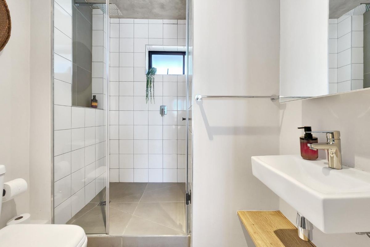 Modern bathroom featuring a walk-in shower with glass screen, wall-mounted basin, and contemporary tiled finishes with an exposed concrete ceiling.