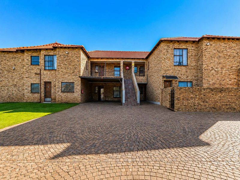 A well-maintained apartment complex featuring a face brick facade, terracotta roof tiles, and a spacious paved driveway with covered parking.