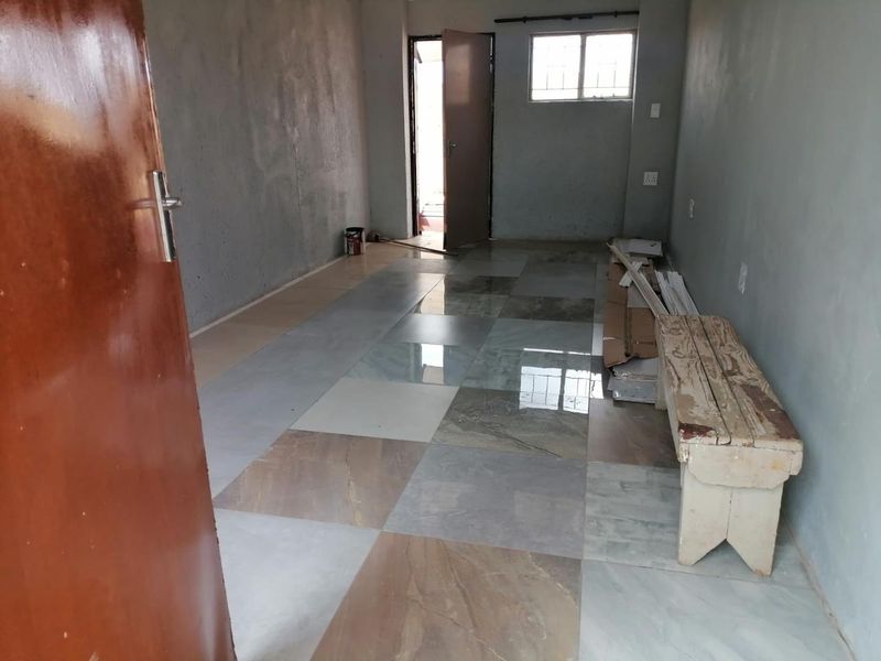 An empty, unfinished living area featuring large format floor tiles and exposed wall surfaces, offering a blank canvas for renovation.