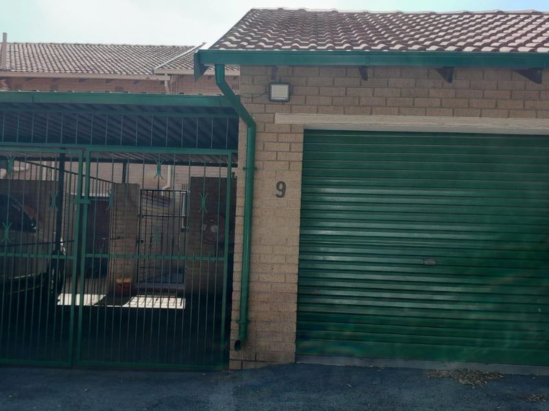Exterior view of a townhouse garage featuring a green roller shutter door and an adjacent gated carport area.