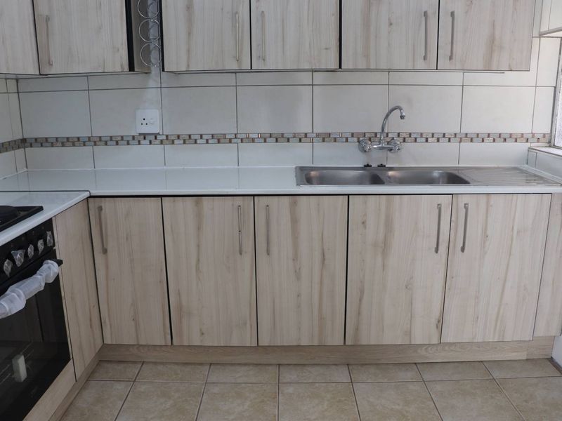 A clean, functional kitchen featuring light wood-finish cabinetry, a double sink, tiled backsplash, and a built-in oven.