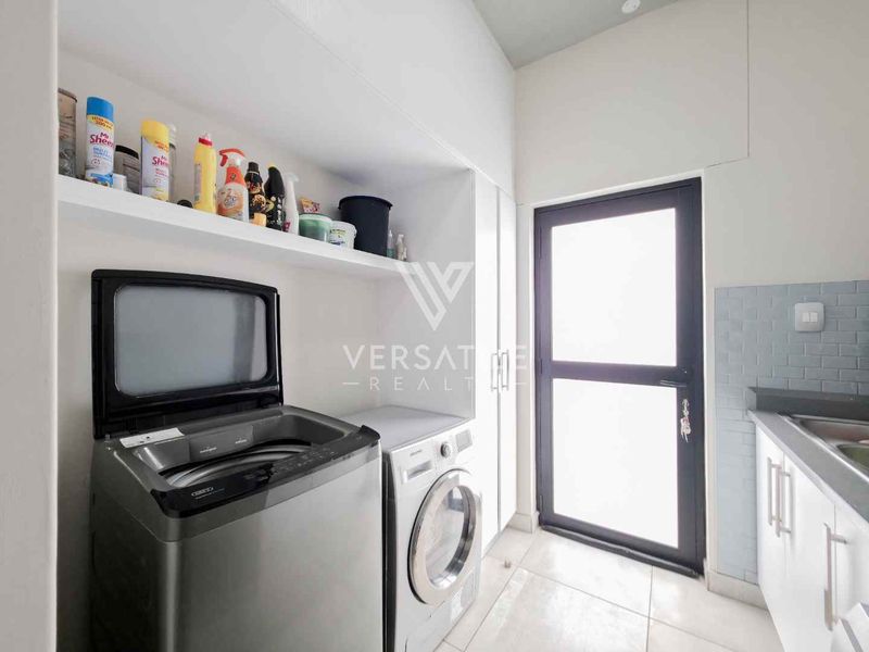 A functional laundry room featuring built-in shelving, tiled flooring, a sink with a subway tile backsplash, and direct access to the exterior.