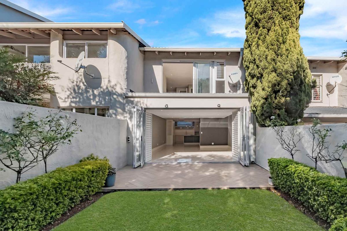 Rear view of the townhouse featuring a landscaped garden, paved patio area, and large bi-fold doors opening into the open-plan living space.