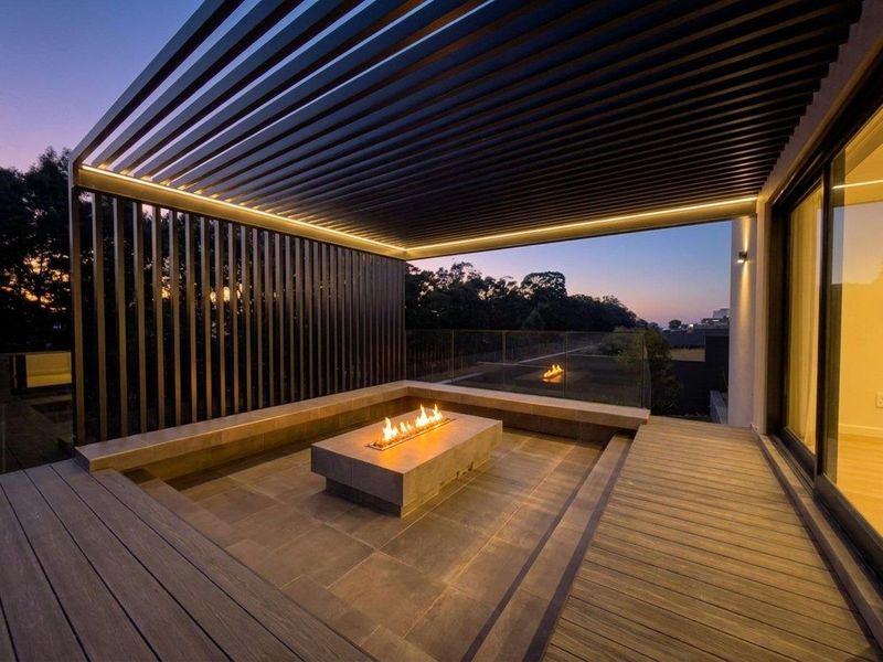 Modern covered patio featuring a sunken seating area with a built-in fire pit, timber decking, and a louvered pergola with integrated lighting.