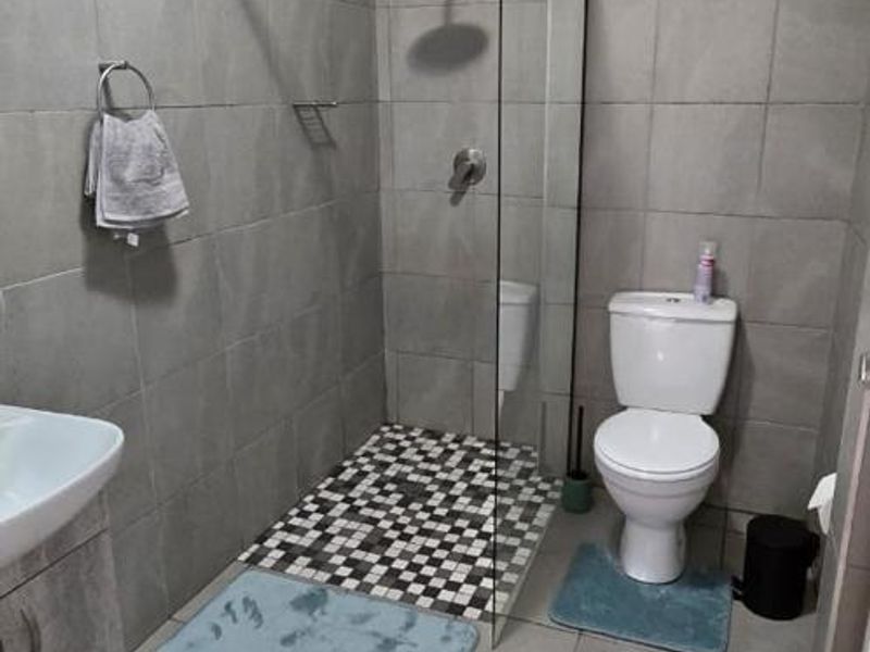 Modern bathroom featuring a walk-in shower with a glass screen, rain shower head, wall-mounted toilet, and a vanity cabinet with grey tiled finishes.