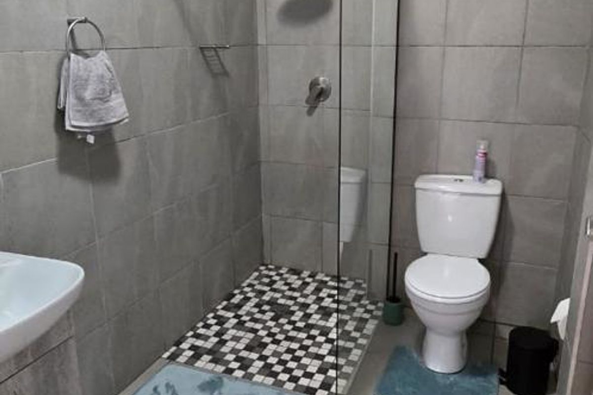 Modern bathroom featuring a walk-in shower with a glass screen, rain shower head, wall-mounted toilet, and a vanity cabinet with grey tiled finishes.