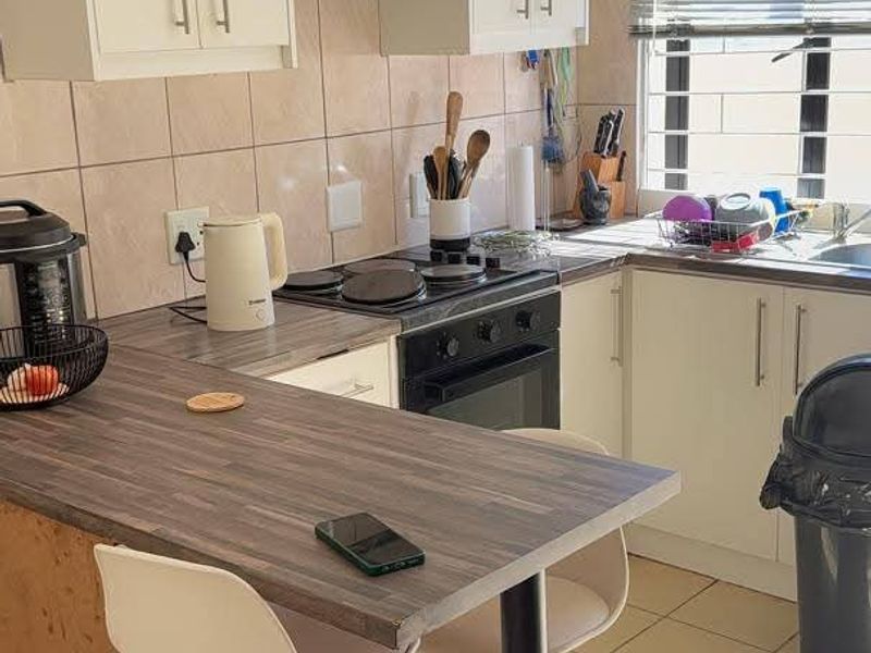 Compact kitchen featuring white cabinetry, laminate countertops, integrated oven and hob, tiled backsplash, and ceramic flooring with natural light from a window.