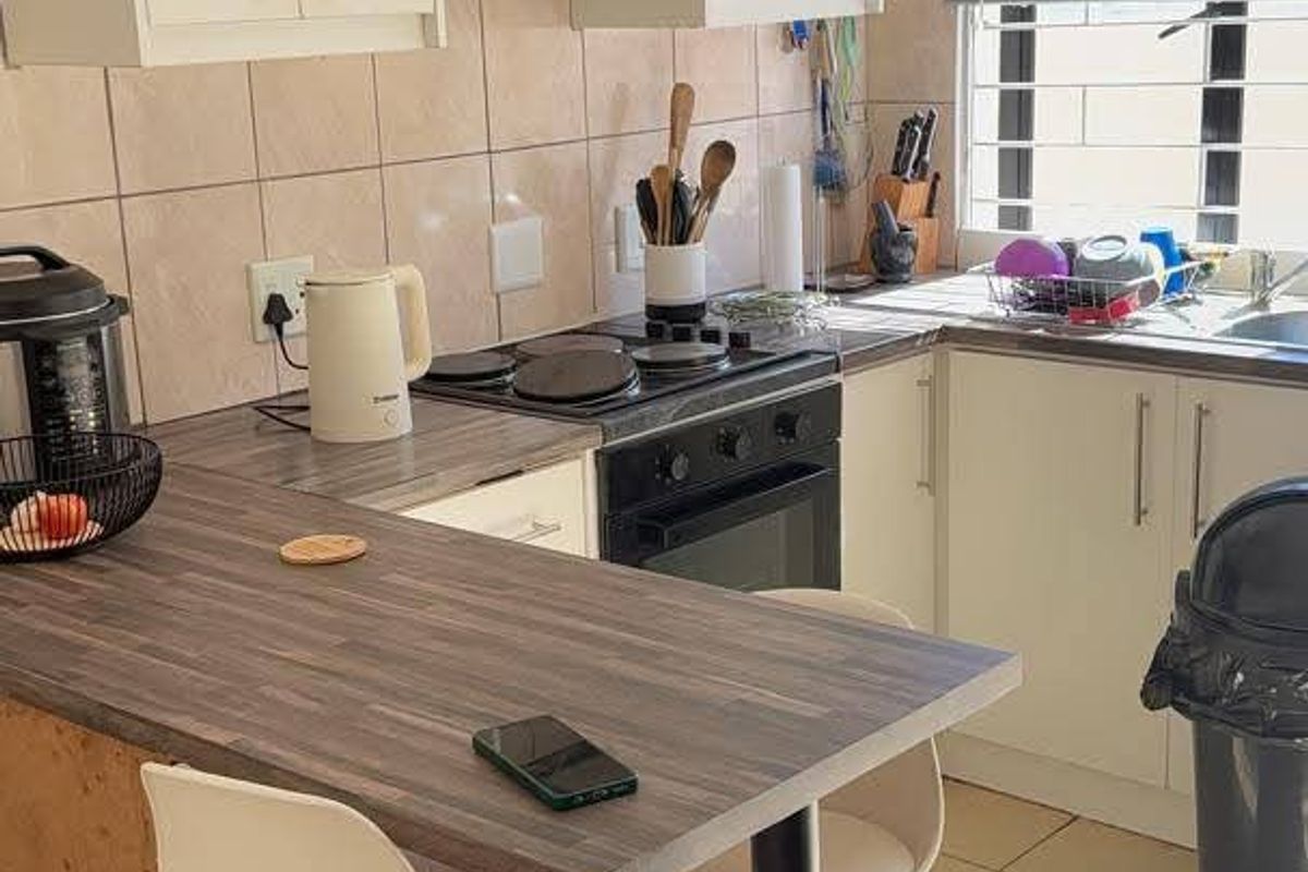 Compact kitchen featuring white cabinetry, laminate countertops, integrated oven and hob, tiled backsplash, and ceramic flooring with natural light from a window.