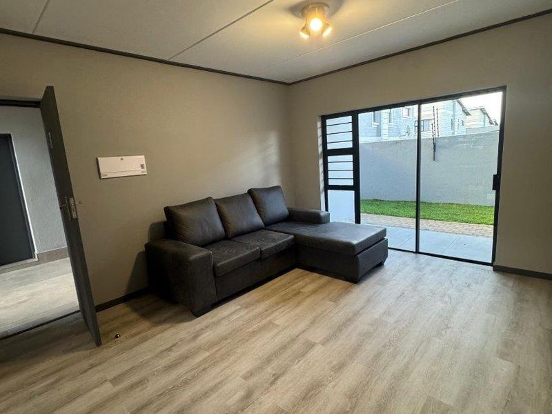 A bright living room featuring modern laminate flooring, neutral wall tones, and a large sliding glass door providing direct access to the outdoor area.