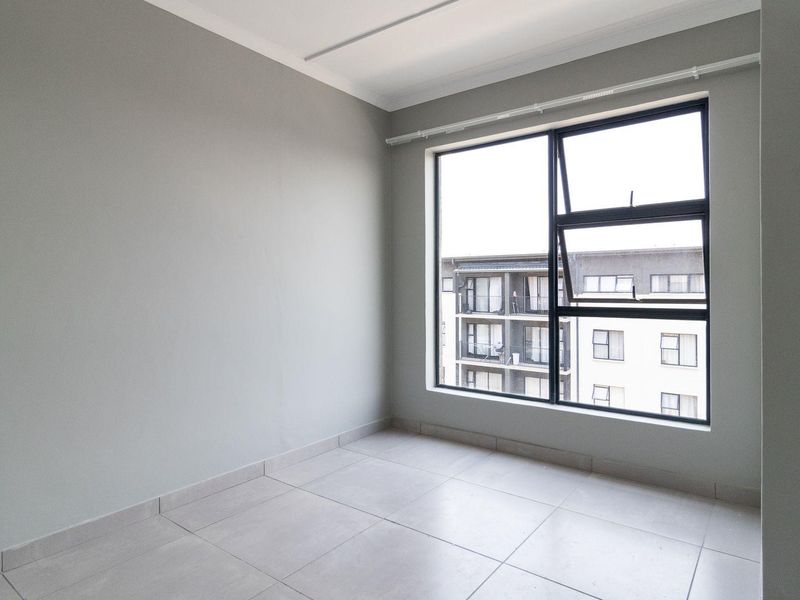 A bright, empty bedroom featuring neutral grey walls, large aluminium-framed windows, and clean tiled flooring, offering a versatile space ready for personalization.