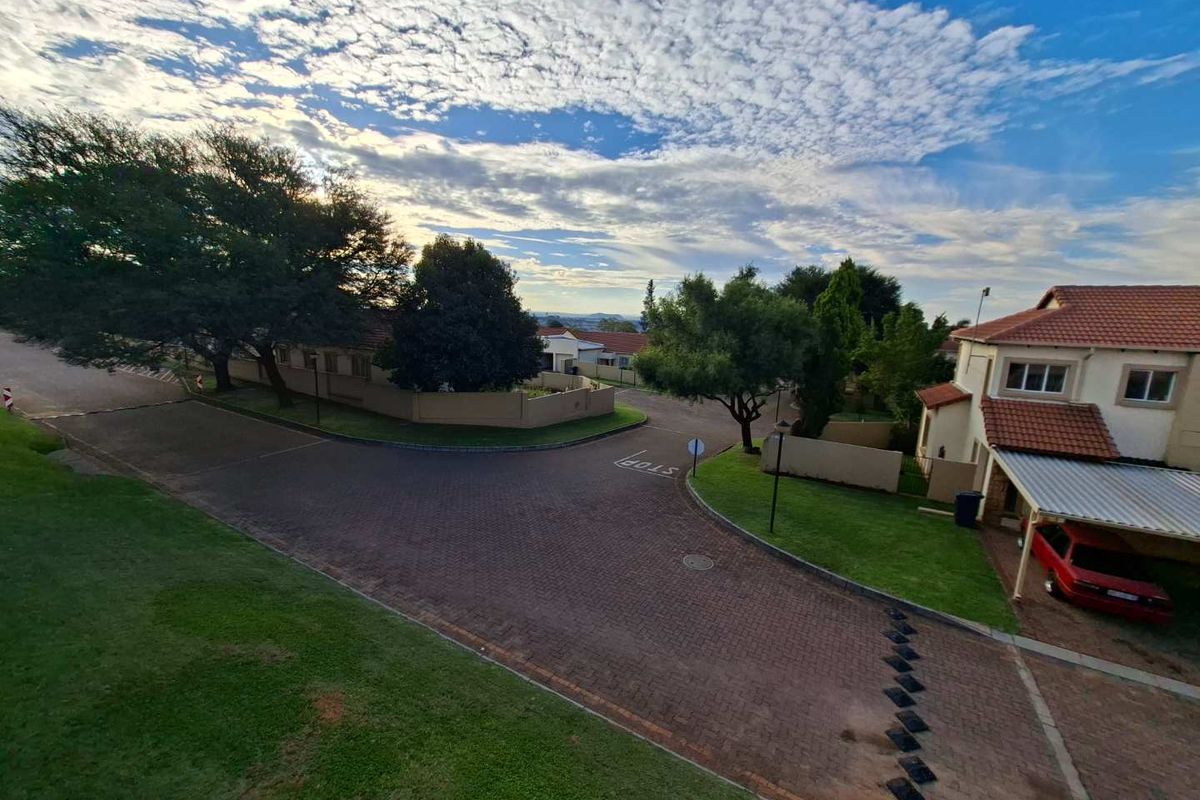 An elevated aerial view of a residential street corner featuring paved driveways, perimeter walls, and established landscaping within a suburban estate.