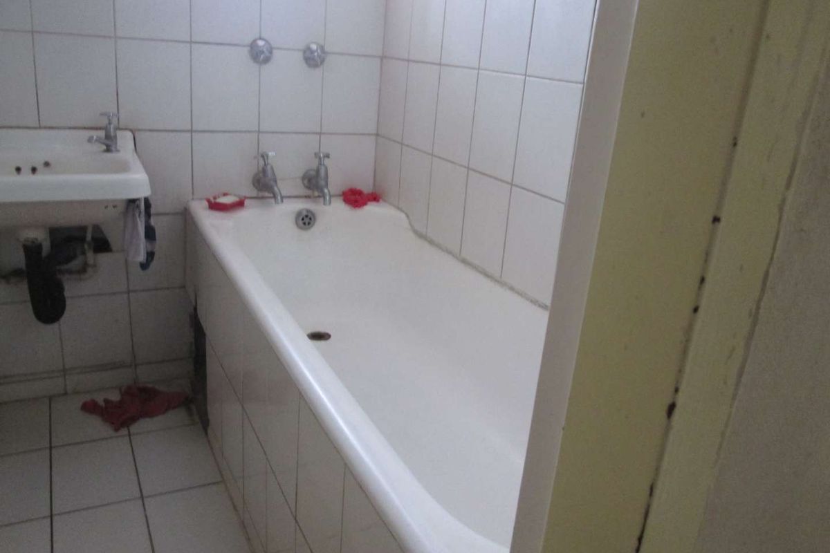 A dated bathroom featuring a standard bathtub, wall-mounted basin, and full-height wall tiling, requiring modernization to improve functionality and aesthetic appeal.