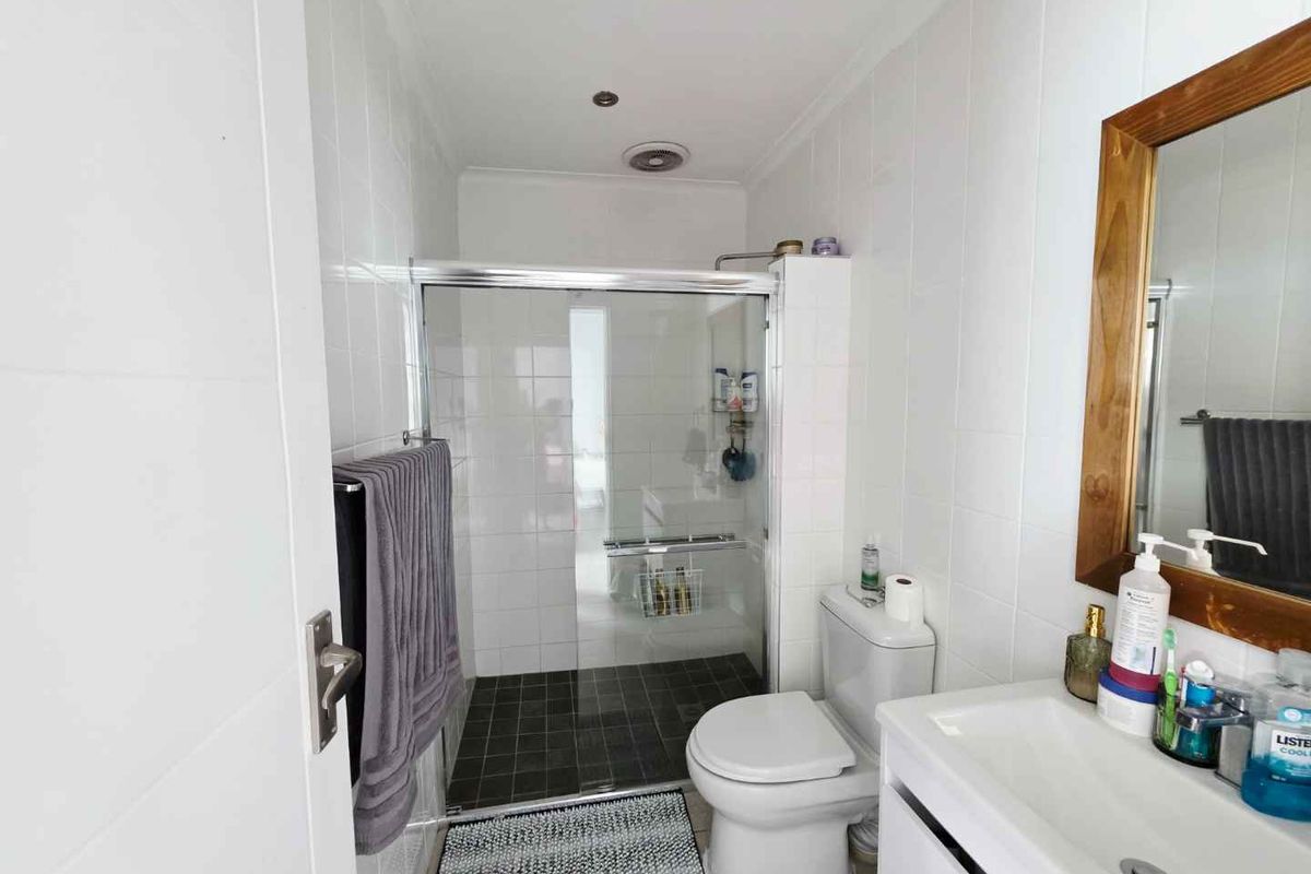 A functional bathroom featuring a glass-enclosed shower, white wall tiling, a vanity basin, and a standard toilet.