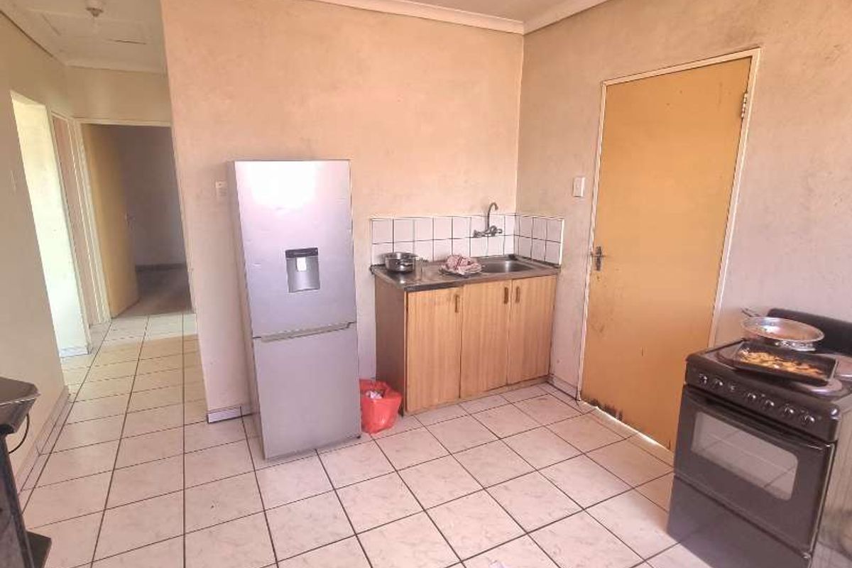 A functional kitchen area featuring basic cabinetry, a stainless steel sink, and tiled flooring, offering potential for modernization and cosmetic updates.