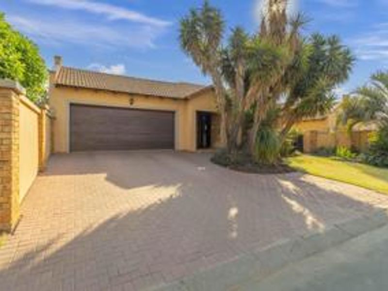 Front elevation of a cluster home featuring a paved driveway, double garage, and established garden.