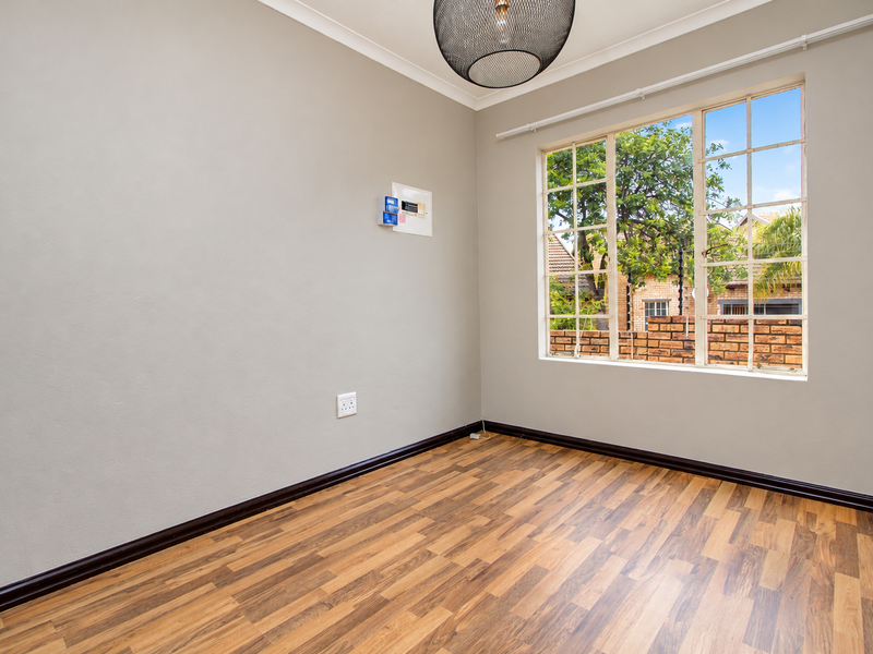 A bright, empty bedroom featuring laminate flooring, neutral walls, and a large multi-pane window overlooking the exterior.