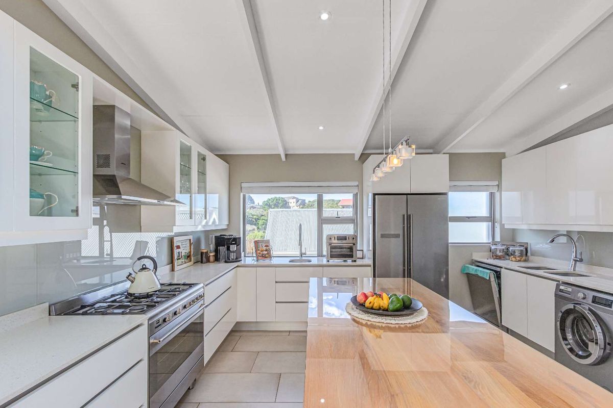 Modern kitchen featuring white cabinetry, stone countertops, a central island, stainless steel gas stove, extractor fan, and integrated appliances.