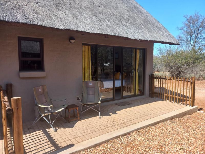 A covered patio area featuring a traditional thatch roof, paved flooring, and sliding glass doors providing access to the interior.