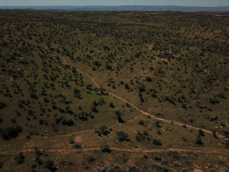 An aerial view of expansive, undeveloped residential land featuring natural vegetation and an unpaved access track.