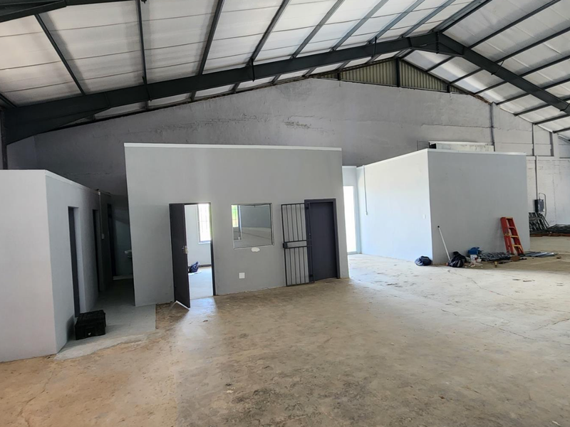 Spacious industrial warehouse featuring high exposed steel roof trusses, concrete flooring, and internal partitioned office spaces with security access.